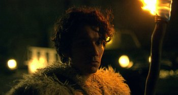 Movie still from “The Field Guide to Evil” (2018), directed by Can Evrenol – A man in a feather boa is looking at the camera; Close Up shot, Over the shoulder angle