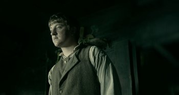 Movie still from “The Field Guide to Evil” (2018), directed by Can Evrenol – A young man in a vest and shirt standing next to a wall; Medium shot, Low angle