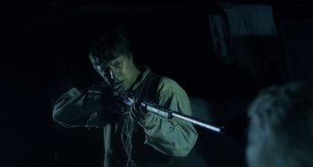 Movie still from “The Field Guide to Evil” (2018), directed by Can Evrenol – A man is holding a rifle in the dark; Medium shot, Low angle