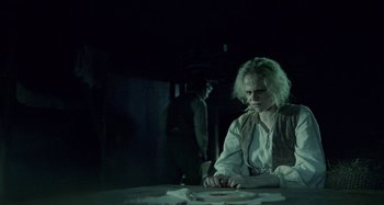 Movie still from “The Field Guide to Evil” (2018), directed by Can Evrenol – A woman sitting at a table in a dimly - lit room; Medium shot, Over the shoulder angle
