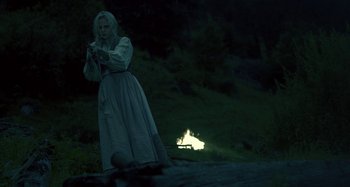 Movie still from “The Field Guide to Evil” (2018), directed by Can Evrenol – A woman standing in the dark near a fire; Medium shot, Over the shoulder angle