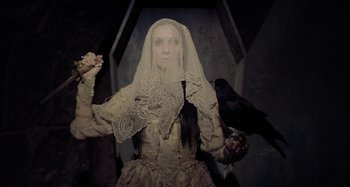 Movie still from “The Field Guide to Evil” (2018), directed by Can Evrenol – A woman wearing a veil and holding a crow; Medium shot, Overhead angle