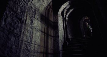 Movie still from “The Field Guide to Evil” (2018), directed by Can Evrenol – A stone archway and a stone staircase in a dark room; Wide shot, Low angle