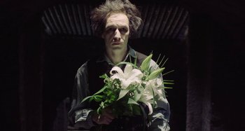 Movie still from “The Field Guide to Evil” (2018), directed by Can Evrenol – A man holding a bouquet of flowers in his hands; Medium shot, Over the shoulder angle