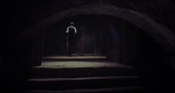 Movie still from “The Field Guide to Evil” (2018), directed by Can Evrenol – A man standing in a dark room holding a cane; Wide shot, Low angle