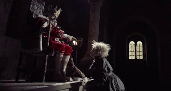 Movie still from “The Field Guide to Evil” (2018), directed by Can Evrenol – A woman sitting on a stage next to a statue of a person; Wide shot, Low angle