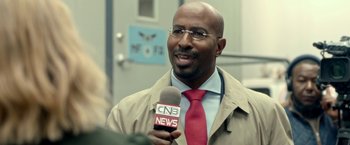Movie still from “The First Purge” (2018), directed by Gerard McMurray – A man in a tan jacket and a red tie holding a microphone; Close Up shot, Over the shoulder angle