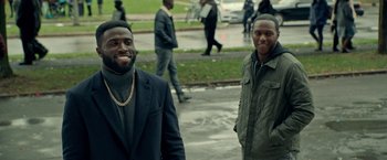 Movie still from “The First Purge” (2018), directed by Gerard McMurray – A couple of men standing next to each other on a sidewalk; Medium shot, Over the shoulder angle