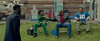 Movie still from “The First Purge” (2018), directed by Gerard McMurray – Two men sitting on a chair and one is holding the arm of the other man; Wide shot, Over the shoulder angle