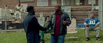 Movie still from “The First Purge” (2018), directed by Gerard McMurray – Two men shaking hands in front of a brick building; Medium shot, Over the shoulder angle