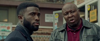 Movie still from “The First Purge” (2018), directed by Gerard McMurray – Two men standing next to each other in front of a brick building; Close Up shot, Low angle