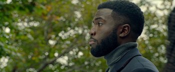 Movie still from “The First Purge” (2018), directed by Gerard McMurray – A person with a beard looking to the side; Close Up shot, Over the shoulder angle