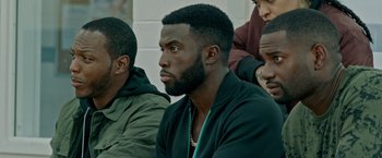 Movie still from “The First Purge” (2018), directed by Gerard McMurray – A group of men sitting next to each other in a room; Close Up shot, Over the shoulder angle