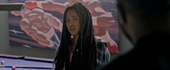 Movie still from “The First Purge” (2018), directed by Gerard McMurray – A woman with long braids standing in front of a painting; Close Up shot, Over the shoulder angle
