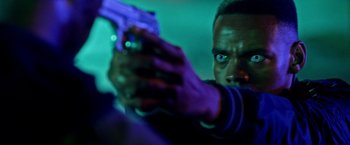 Movie still from “The First Purge” (2018), directed by Gerard McMurray – A man holding a gun in a room with neon lights; Close Up shot, Over the shoulder angle