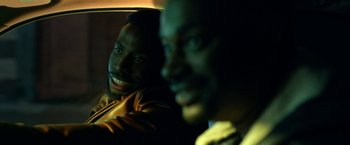 Movie still from “The First Purge” (2018), directed by Gerard McMurray – Two men smile for the camera in the back of a car; Close Up shot, Over the shoulder angle