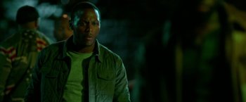 Movie still from “The First Purge” (2018), directed by Gerard McMurray – A man standing in the dark wearing a green shirt; Close Up shot, Over the shoulder angle