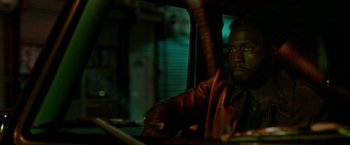 Movie still from “The First Purge” (2018), directed by Gerard McMurray – A man sitting in the driver's seat of a car; Medium shot, Over the shoulder angle