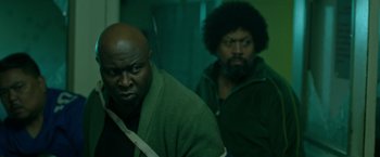 Movie still from “The First Purge” (2018), directed by Gerard McMurray – Two men are standing next to each other in a room; Medium shot, Over the shoulder angle