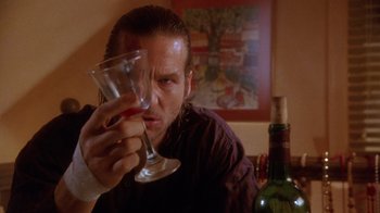 Movie still from “The Fisher King” (1991), directed by Terry Gilliam – A man sitting at a table holding a wine glass in front of a bottle; Close Up shot, Low angle