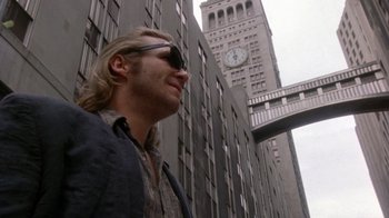 Movie still from “The Fisher King” (1991), directed by Terry Gilliam – A man standing in front of a tall building with a clock; Medium shot, Low angle
