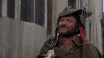 Movie still from “The Fisher King” (1991), directed by Terry Gilliam – A man in a cowboy hat holding a dollar bill in front of a building; Medium shot, Low angle