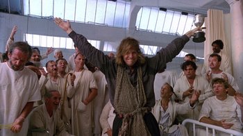 Movie still from “The Fisher King” (1991), directed by Terry Gilliam – A group of people standing in a room with one person raising his hands; Wide shot, Low angle
