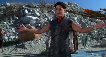 Movie still from “The Flintstones” (1994), directed by Brian Levant – A man wearing a vest and holding something in his hand; Medium shot, Low angle