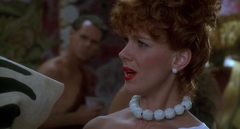Movie still from “The Flintstones” (1994), directed by Brian Levant – A person wearing a necklace with a man in the background; Close Up shot, Over the shoulder angle