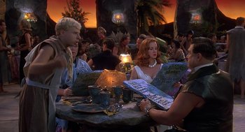 Movie still from “The Flintstones” (1994), directed by Brian Levant – A group of people sitting around a table; Medium shot, Over the shoulder angle