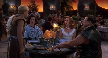 Movie still from “The Flintstones” (1994), directed by Brian Levant – A group of people sitting at a table with plates; Medium shot, Over the shoulder angle