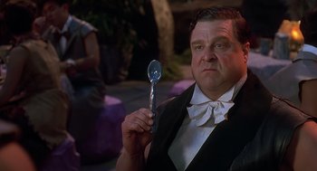 Movie still from “The Flintstones” (1994), directed by Brian Levant – A man in a tuxedo holding a spoon in his hand; Medium shot, Over the shoulder angle