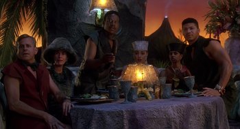 Movie still from “The Flintstones” (1994), directed by Brian Levant – A group of people sitting at a table with food; Medium shot, High angle