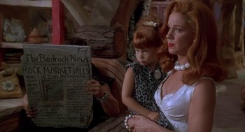 Movie still from “The Flintstones” (1994), directed by Brian Levant – A woman sitting next to a young girl holding a newspaper; Medium shot, Over the shoulder angle
