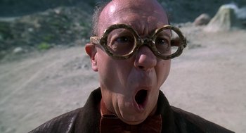 Movie still from “The Flintstones” (1994), directed by Brian Levant – An old man wearing glasses and a bow tie making a funny face; Close Up shot, Low angle