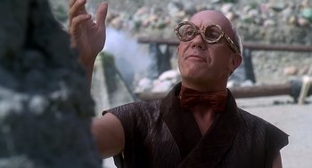 Movie still from “The Flintstones” (1994), directed by Brian Levant – A bald man wearing glasses and a bow tie; Close Up shot, Low angle
