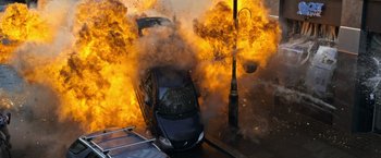 Movie still from “The Foreigner” (2017), directed by Martin Campbell – A car that is on fire in the street; Extreme Wide shot, Overhead angle