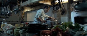 Movie still from “The Foreigner” (2017), directed by Martin Campbell – A man in a white shirt is cooking in a kitchen; Medium shot, Low angle