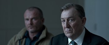 Movie still from “The Foreigner” (2017), directed by Martin Campbell – A man in a suit and tie standing next to another man; Close Up shot, Over the shoulder angle