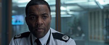 Movie still from “The Foreigner” (2017), directed by Martin Campbell – A person wearing a police uniform; Close Up shot, Over the shoulder angle