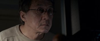 Movie still from “The Foreigner” (2017), directed by Martin Campbell – An older man wearing glasses looking at the camera; Close Up shot, Over the shoulder angle