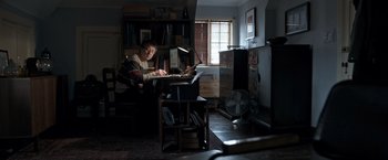 Movie still from “The Foreigner” (2017), directed by Martin Campbell – A man sitting at a table with a laptop; Wide shot, High angle