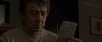 Movie still from “The Foreigner” (2017), directed by Martin Campbell – An older man holding a piece of paper in front of his face; Close Up shot, Low angle