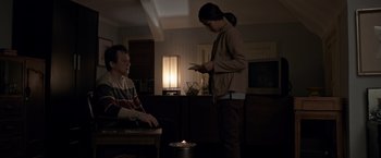 Movie still from “The Foreigner” (2017), directed by Martin Campbell – A man and a woman in a dark living room; Medium shot, High angle