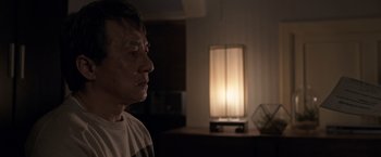 Movie still from “The Foreigner” (2017), directed by Martin Campbell – A man standing in front of a lamp in a dark room; Close Up shot, Over the shoulder angle