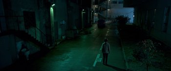 Movie still from “The Foreigner” (2017), directed by Martin Campbell – A person standing on a street at night; Extreme Wide shot, High angle