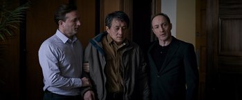 Movie still from “The Foreigner” (2017), directed by Martin Campbell – A group of men standing next to each other in a room; Medium shot, High angle
