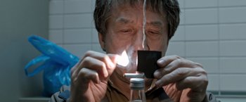 Movie still from “The Foreigner” (2017), directed by Martin Campbell – An older man lighting a candle in a jar; Close Up shot, High angle