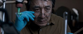 Movie still from “The Foreigner” (2017), directed by Martin Campbell – An older man wearing glasses and wearing a blue glove; Close Up shot, Low angle