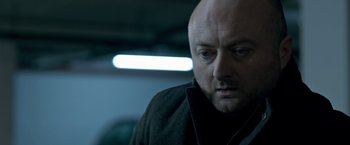Movie still from “The Foreigner” (2017), directed by Martin Campbell – A man with a bald head looking down at the ground; Close Up shot, Low angle